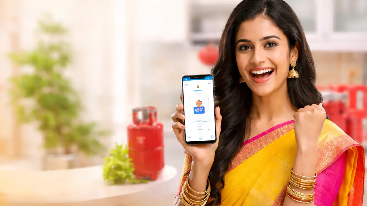 Young South Indian woman happily booking LPG gas cylinder online using mobile phone in kitchen